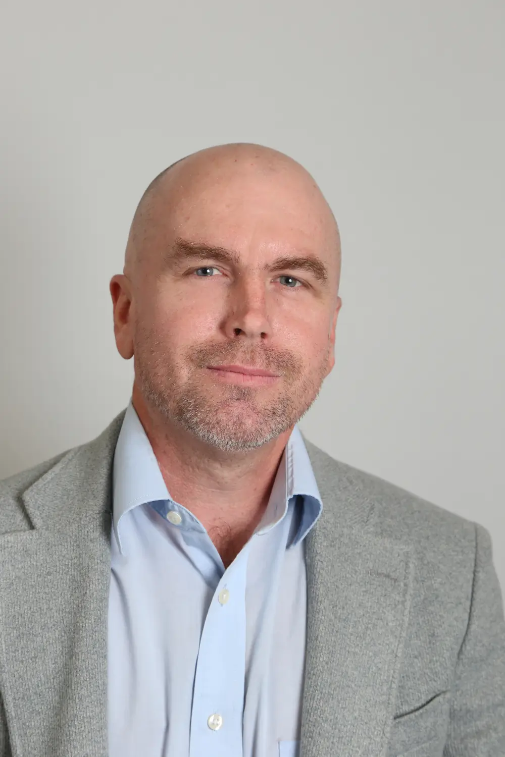 Professional headshot of bald man in gray blazer
